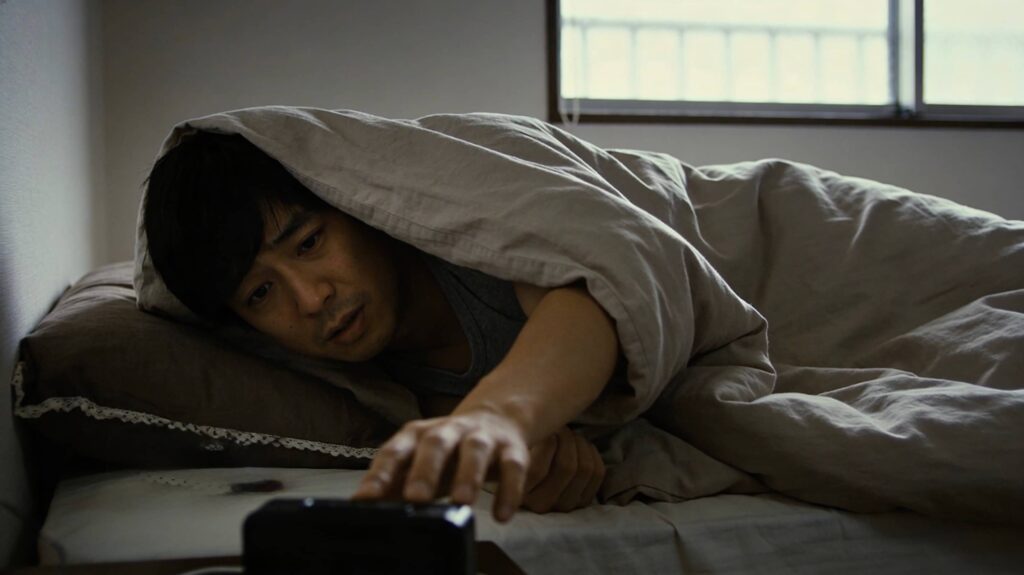 朝、ベッドから出られない男性の画像。朝の弱さを表している。